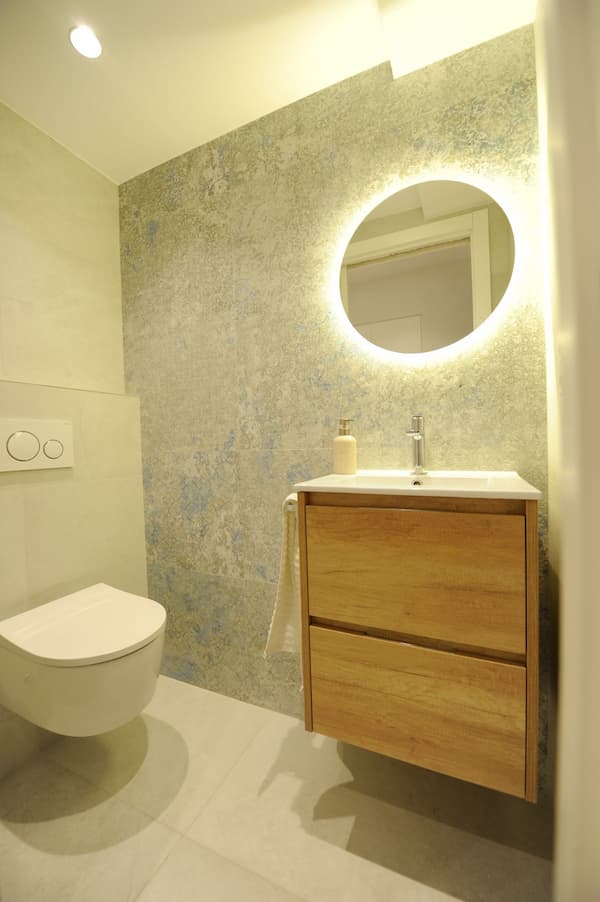Reforma de pequeño baño con espejo redondo e inodoro suspendido en el barrio de Amara Donosti